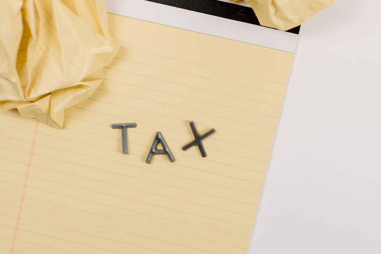 Close-up of a yellow lined paper with metal letters spelling tax, surrounded by crumpled paper.